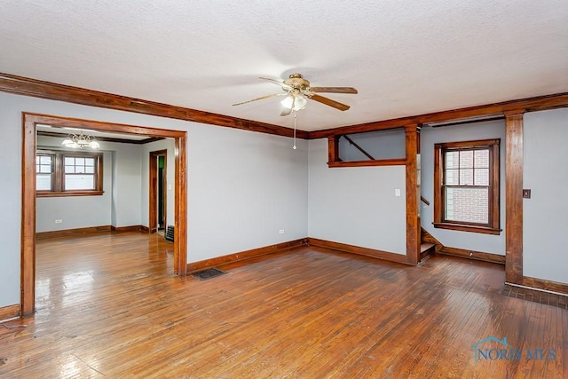 spare room with a healthy amount of sunlight, ceiling fan with notable chandelier, and hardwood / wood-style flooring