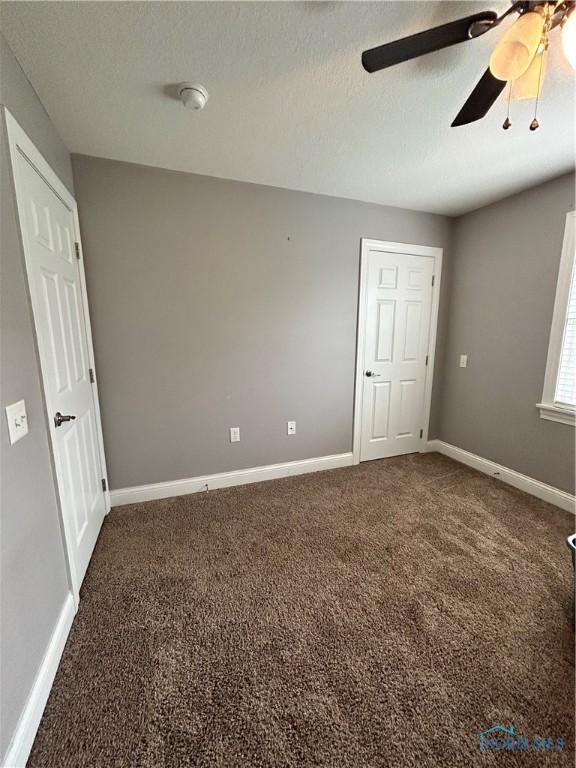 unfurnished bedroom featuring dark colored carpet, ceiling fan, and a textured ceiling