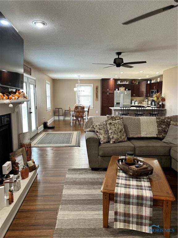 living room featuring a textured ceiling, ceiling fan with notable chandelier, and dark wood-type flooring