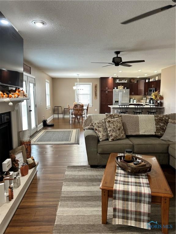 living room featuring ceiling fan, a textured ceiling, dark hardwood / wood-style floors, and a healthy amount of sunlight