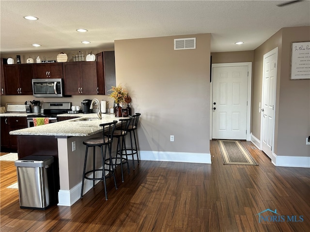 kitchen with dark hardwood / wood-style flooring, a textured ceiling, stainless steel appliances, sink, and a breakfast bar area