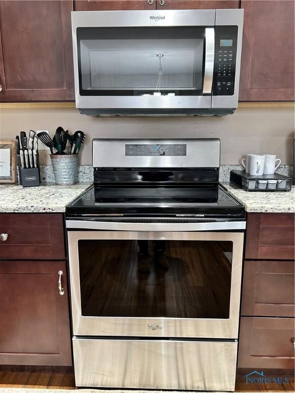 kitchen featuring stainless steel appliances, light stone countertops, and dark brown cabinets