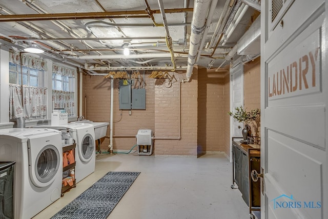 laundry room featuring electric panel, washing machine and dryer, and brick wall