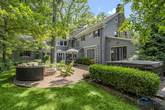 back of property with a hot tub, a fire pit, a yard, and a patio area