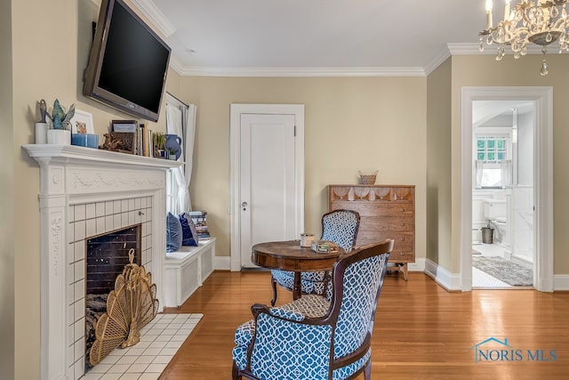 living area with a tile fireplace, hardwood / wood-style flooring, ornamental molding, and a notable chandelier