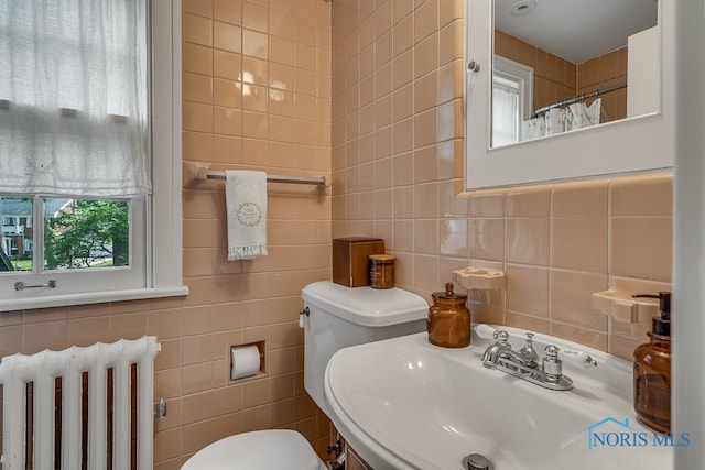 bathroom with sink, radiator heating unit, tile walls, and toilet