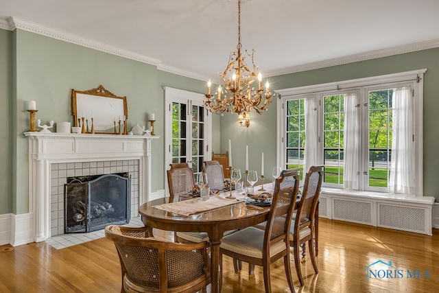 dining room featuring ornamental molding, light hardwood / wood-style floors, a chandelier, and a tile fireplace