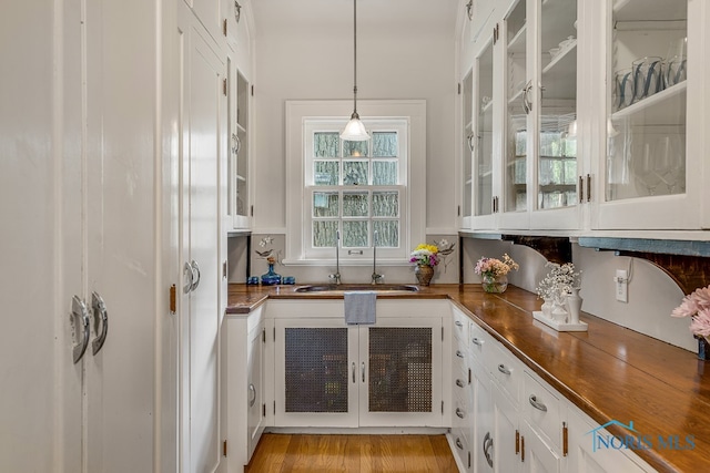 kitchen featuring white cabinets, light wood-type flooring, sink, and pendant lighting