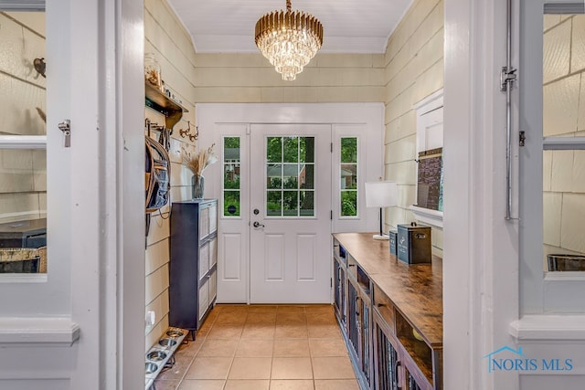 entryway with wood walls, light tile patterned floors, and an inviting chandelier