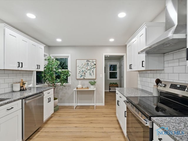 kitchen featuring white cabinetry, stainless steel appliances, wall chimney range hood, and light stone countertops