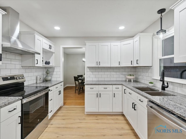 kitchen featuring stainless steel appliances, white cabinetry, wall chimney range hood, sink, and light hardwood / wood-style floors