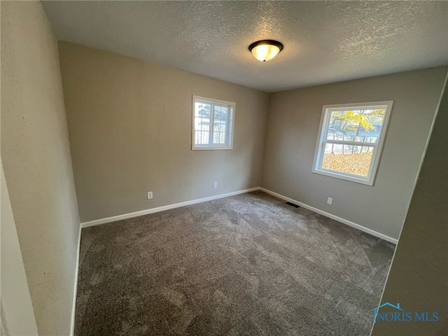 empty room with dark colored carpet and a textured ceiling