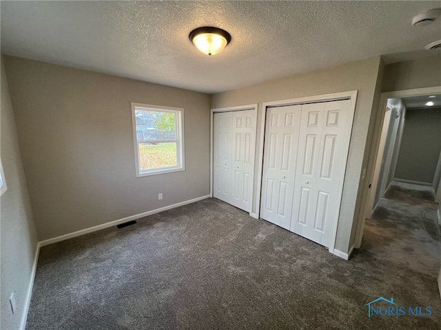 unfurnished bedroom with dark colored carpet, a textured ceiling, and multiple closets