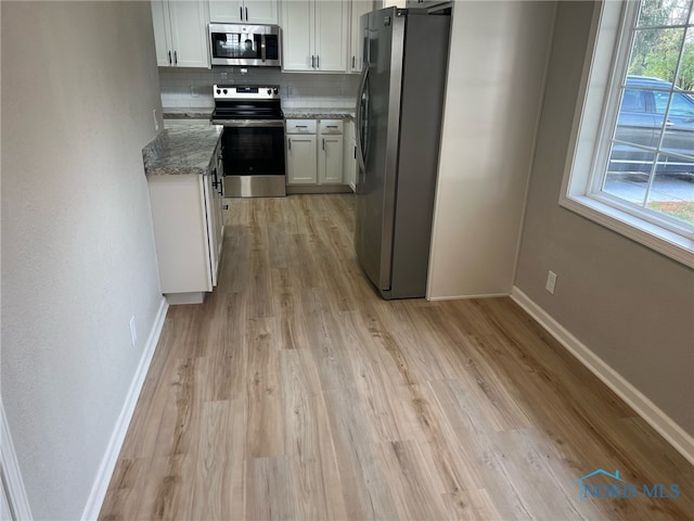 kitchen featuring light wood-type flooring, backsplash, stainless steel appliances, stone counters, and white cabinets