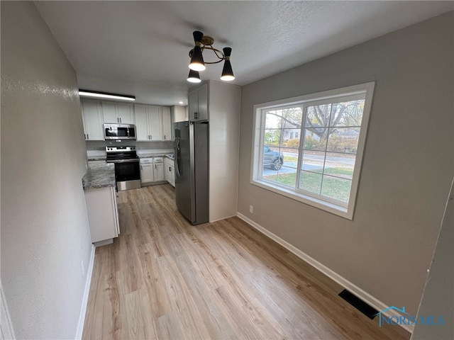 kitchen with white cabinets, dark stone countertops, light wood-type flooring, and appliances with stainless steel finishes