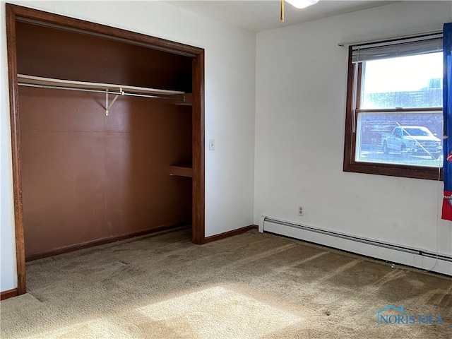 unfurnished bedroom with a closet, baseboard heating, and carpet floors