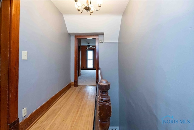 corridor featuring light hardwood / wood-style flooring, a notable chandelier, and vaulted ceiling