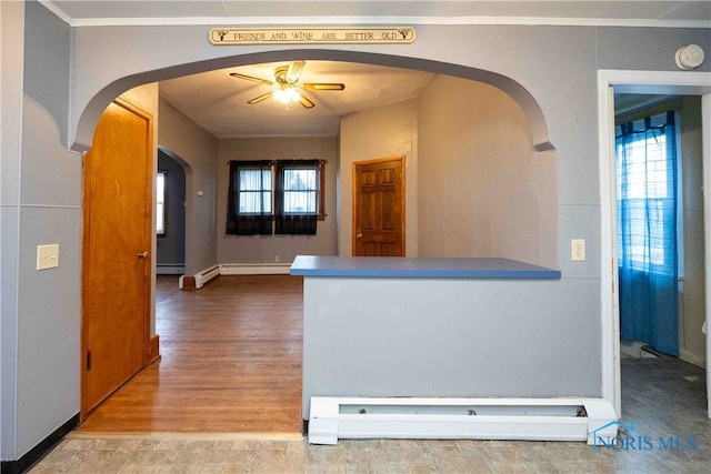 kitchen with baseboard heating, hardwood / wood-style floors, ceiling fan, and crown molding