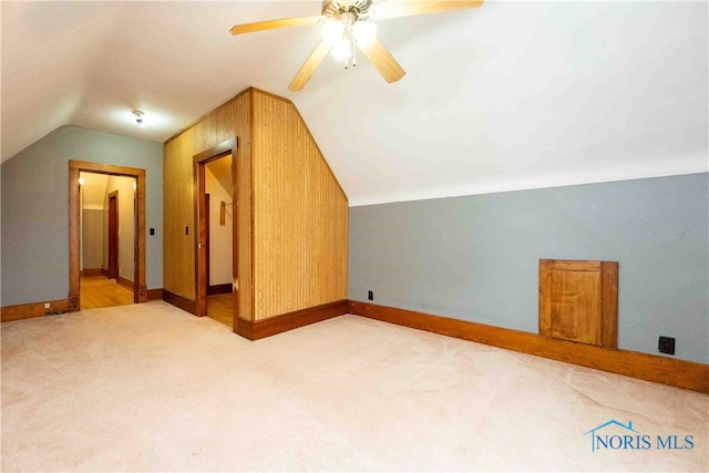 additional living space with wood walls, lofted ceiling, light carpet, and ceiling fan