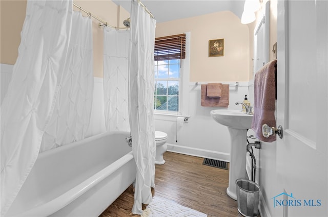 bathroom with hardwood / wood-style floors, toilet, and shower / bathtub combination with curtain