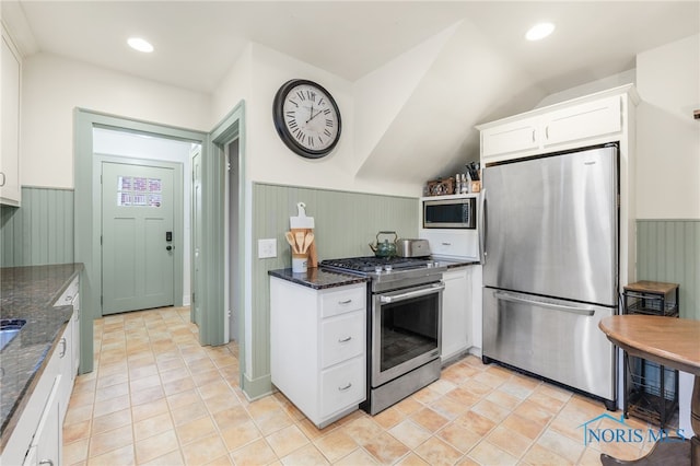 kitchen with dark stone counters, vaulted ceiling, light tile patterned floors, appliances with stainless steel finishes, and white cabinetry