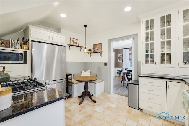 kitchen featuring appliances with stainless steel finishes, light wood-type flooring, dark stone counters, decorative light fixtures, and white cabinetry