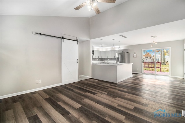 unfurnished living room featuring dark hardwood / wood-style flooring, high vaulted ceiling, a barn door, and ceiling fan