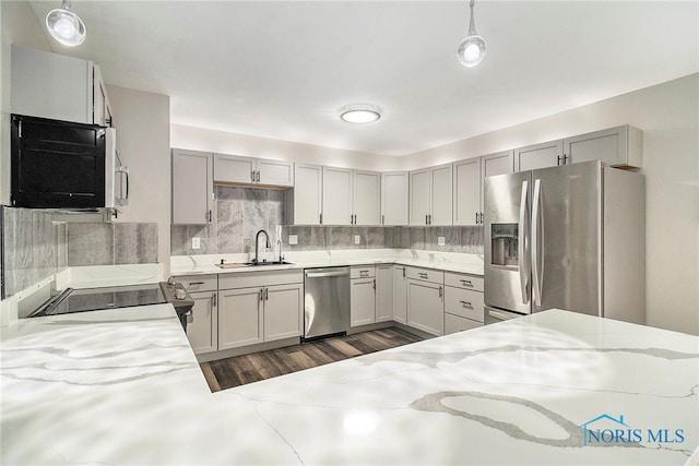 kitchen with pendant lighting, tasteful backsplash, sink, light stone counters, and stainless steel appliances