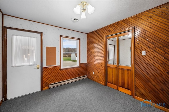 spare room with carpet, wooden walls, and a baseboard heating unit