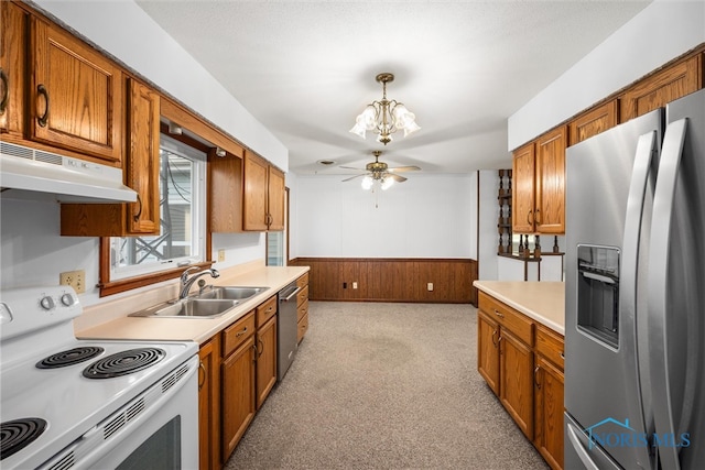 kitchen featuring ceiling fan with notable chandelier, stainless steel appliances, wooden walls, sink, and pendant lighting