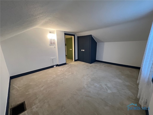 additional living space with a textured ceiling, light carpet, and lofted ceiling