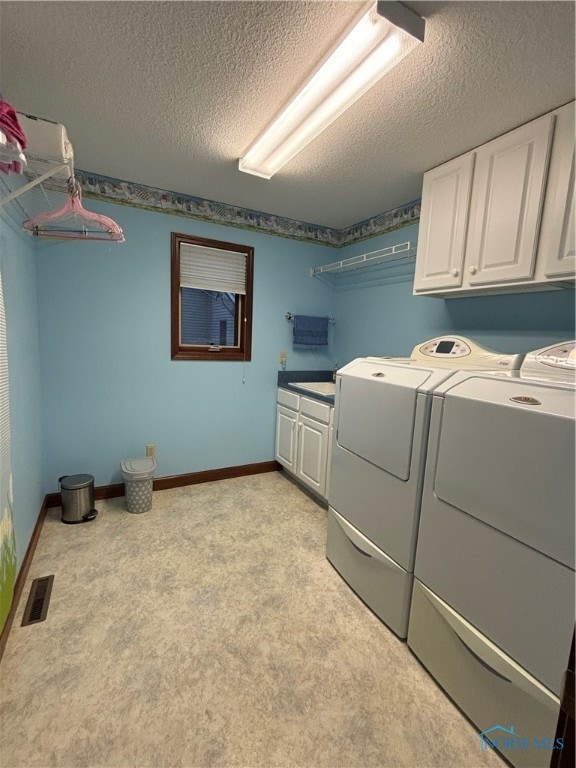 clothes washing area with cabinets, light colored carpet, a textured ceiling, and washing machine and dryer