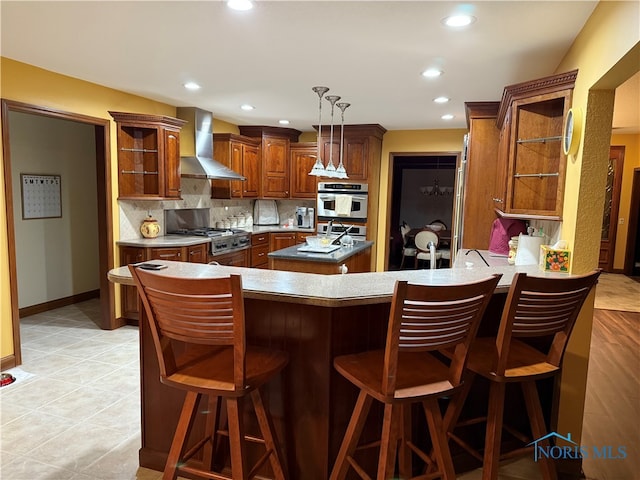 kitchen featuring wall chimney exhaust hood, kitchen peninsula, a breakfast bar area, and stainless steel appliances