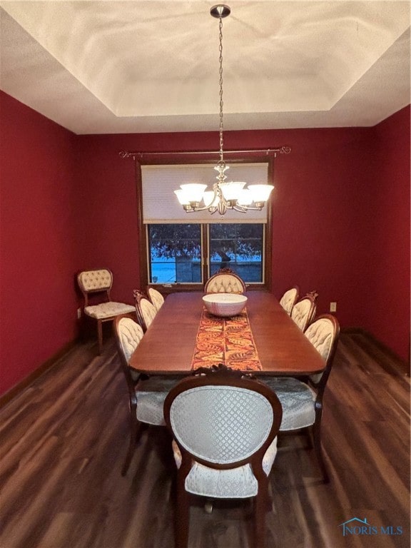 dining area with wood-type flooring, a tray ceiling, and a notable chandelier