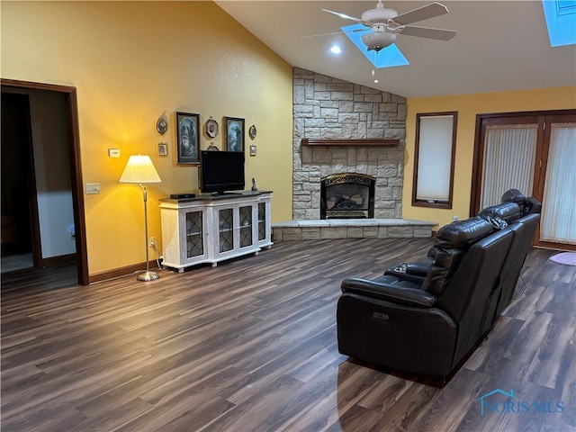 living room with vaulted ceiling, ceiling fan, dark wood-type flooring, and a stone fireplace