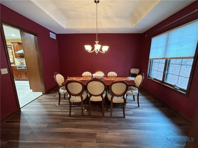 dining space with a tray ceiling, dark hardwood / wood-style flooring, and a notable chandelier