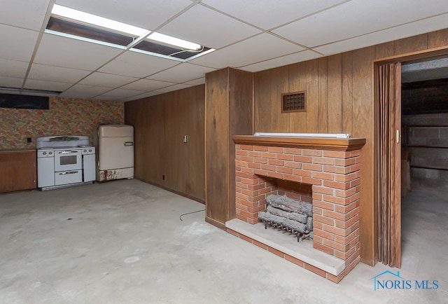 basement with a drop ceiling, a fireplace, fridge, and wood walls