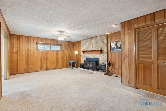 unfurnished living room with a wood stove, wood walls, ceiling fan, and light colored carpet