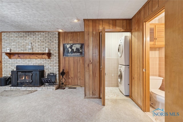 carpeted living room featuring a wood stove, wood walls, stacked washing maching and dryer, and tile walls