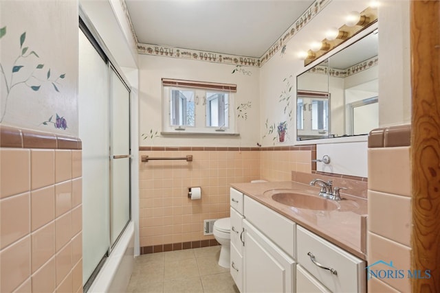 full bathroom featuring tile patterned floors, vanity, shower / bath combination with glass door, tile walls, and toilet