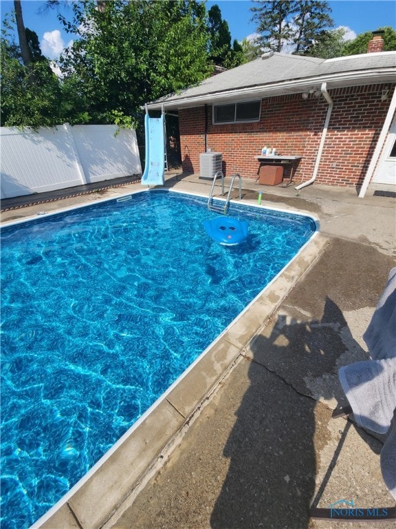 view of swimming pool featuring cooling unit, a water slide, and a patio