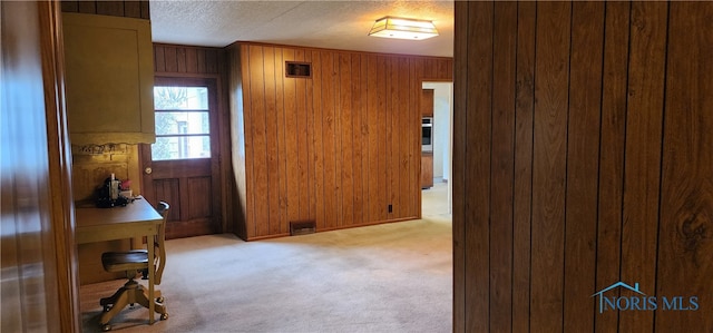 carpeted entryway with wooden walls and a textured ceiling