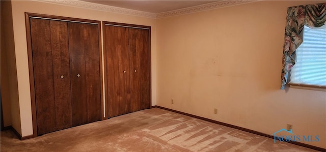 unfurnished bedroom featuring light colored carpet, crown molding, and multiple closets