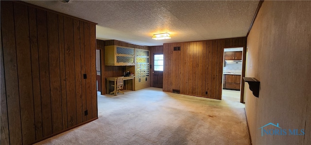 living room with light carpet, wooden walls, built in desk, and a textured ceiling