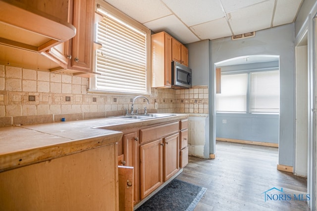 kitchen featuring a paneled ceiling, backsplash, sink, tile countertops, and light hardwood / wood-style floors