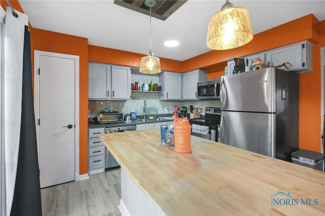 kitchen featuring butcher block counters, light hardwood / wood-style flooring, hanging light fixtures, and appliances with stainless steel finishes