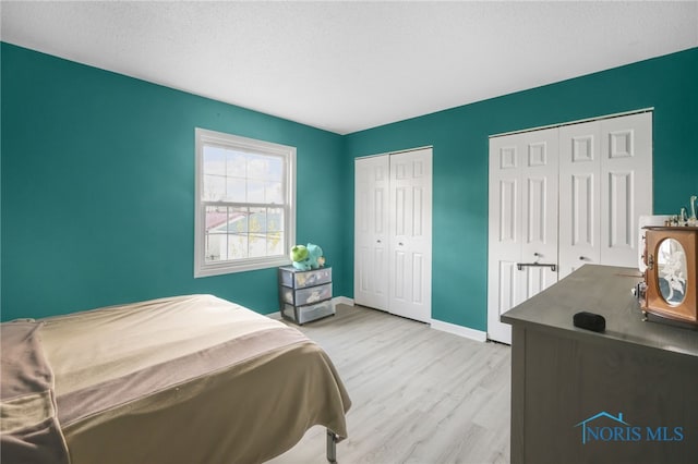 bedroom featuring light hardwood / wood-style floors, a textured ceiling, and two closets