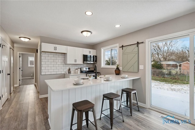 kitchen with kitchen peninsula, stainless steel appliances, a barn door, light hardwood / wood-style flooring, and white cabinets