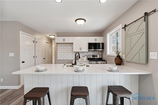 kitchen with sink, a breakfast bar area, a barn door, white cabinetry, and stainless steel appliances