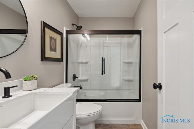 full bathroom featuring shower / bath combination with glass door, hardwood / wood-style floors, vanity, and toilet